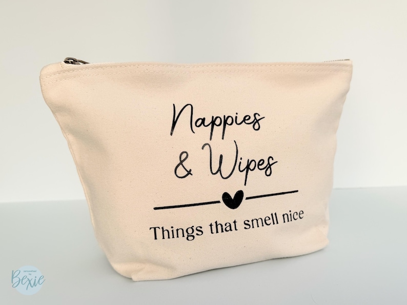 Peut inclure: Un sac en toile beige avec une fermeture &eacute;clair noire. Le sac porte l'inscription "Nappies & Wipes" au-dessus d'un c&oelig;ur et la phrase "Things that smell nice". Con&ccedil;u pour les essentiels de b&eacute;b&eacute;.