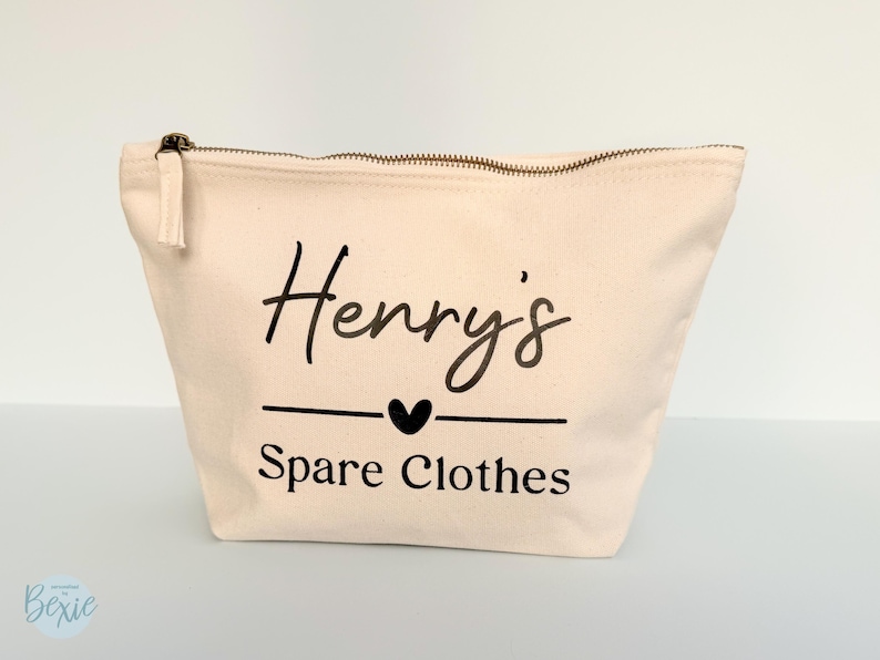 Peut inclure: Une trousse zipp&eacute;e en toile beige avec le nom "Henry's" en &eacute;criture noire, un c&oelig;ur et les mots "Spare Clothes". La trousse a une tirette de fermeture &eacute;clair &agrave; pompon.