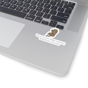 May include: A die-cut sticker featuring a brown cartoon otter floating on its back with the text: YOU HOLD MY HAND THROUGH TURBULENCE YOU SUGARCOAT THE OXYGEN. The sticker is placed on the silver surface of a laptop near the keyboard area.