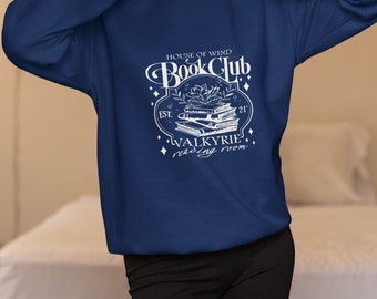Może przedstawiać: Bordowy sweter z białym nadrukiem, na którym widnieje napis "House of Wind Book Club Est. 21, Valkyrie Reading Room". Nadruk przedstawia stos książek z kwiatem i liśćmi.