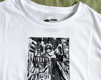 May include: White crew neck t-shirt with a black and white graphic print. The print features a stylized, abstract image of a face or figure. The shirt is made of a soft, likely cotton material.