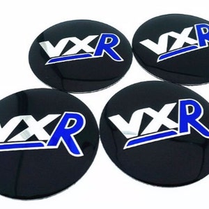 May include: Four black round car wheel centre caps with a silver and blue "VXR" logo.