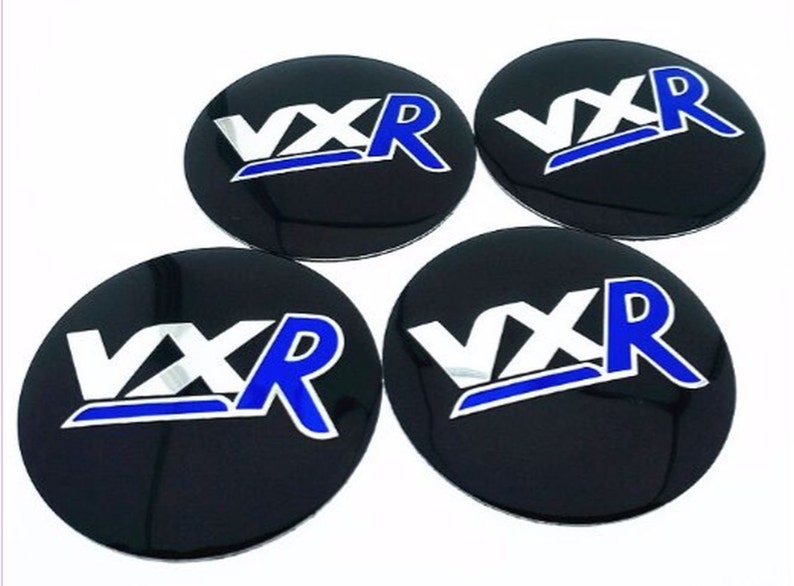 May include: Four black round car wheel centre caps with a silver and blue "VXR" logo.