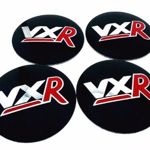 May include: Set of four black round car wheel centre caps with a silver and red "VXR" logo.