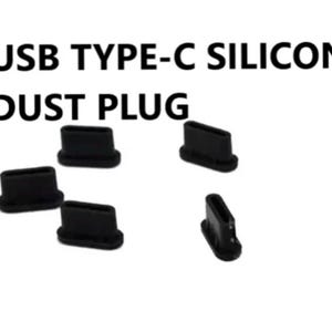 May include: Black silicone USB Type-C dust plugs. Several small, rectangular plugs are shown, designed to protect USB-C ports from dust and debris. The text "USB TYPE-C SILICONE DUST PLUG" is displayed above the plugs.