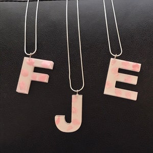 May include: Three silver chain necklaces with pink letter pendants. The letters are F, J, and E. The letters are white with pink polka dots.