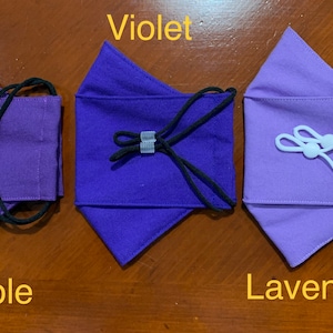 May include: Three fabric face masks in different shades of purple: purple, violet, and lavender. Each mask has a gathered top and adjustable elastic ear loops.