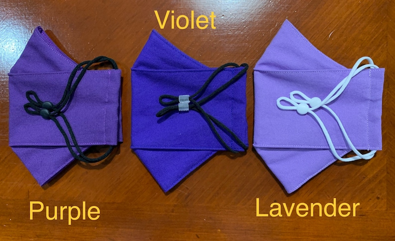 May include: Three fabric face masks in different shades of purple: purple, violet, and lavender. Each mask has a gathered top and adjustable elastic ear loops.