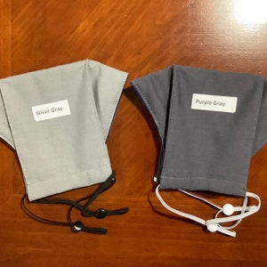 May include: Two fabric face masks, one silver gray and one purple gray, with adjustable ear loops. The masks have labels that say "Silver Gray" and "Purple Gray".