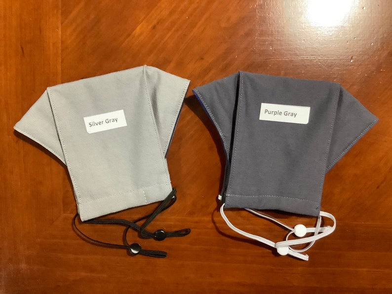 May include: Two fabric face masks, one silver gray and one purple gray, with adjustable ear loops. The masks have labels that say "Silver Gray" and "Purple Gray".