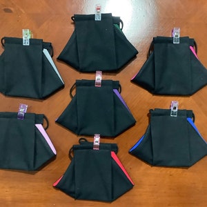 May include: Seven black fabric face masks with different colored trim. The masks are folded and secured with clips.