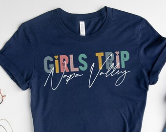 May include: A navy blue t-shirt with the text "Girls Trip Napa Valley" in colorful letters. The text is in a retro style with a heart symbol.