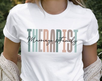 Puede incluir: Camiseta blanca con el texto "Therapist Marriage & Family" en rayas verticales de colores.