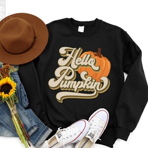 May include: Black sweatshirt with a graphic of a pumpkin and the text "Hello Pumpkin" in a retro font.