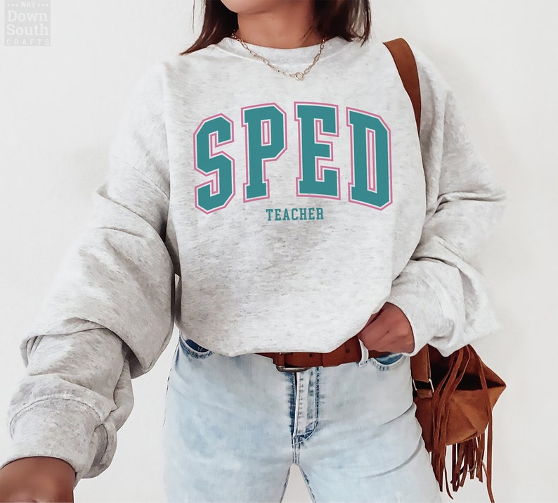 K&ouml;nnte beinhalten: Ein grauer Pullover mit dem Text "SPED TEACHER" in t&uuml;rkisfarbener und rosafarbener Schrift.