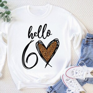 May include: White sweatshirt with black text that says "hello 6" with a leopard print heart.
