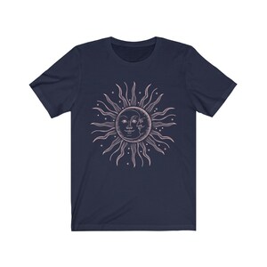 May include: A navy blue t-shirt with a pink sun and moon graphic. The sun and moon are stylized with faces and surrounded by stars.