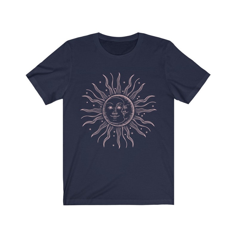 May include: A navy blue t-shirt with a pink sun and moon graphic. The sun and moon are stylized with faces and surrounded by stars.