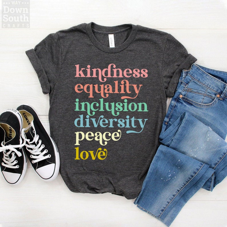 Op de afbeelding: Een donkergrijs T-shirt met de woorden "kindness", "equality", "inclusion", "diversity", "peace" en "love" in kleurrijke letters.