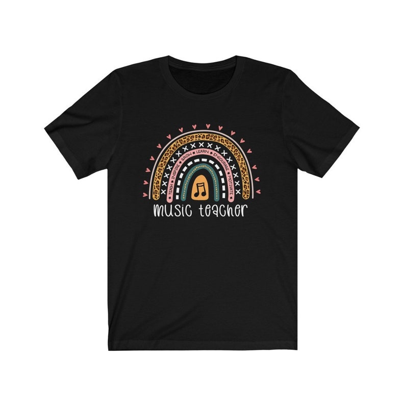 以下が含まれることがあります： 虹のデザインが施された黒いTシャツ。虹には「Today, Inspire, Teach, Sing, Learn, Encourage, Positive」という文字と音符が描かれている。「music teacher」という文字が虹の下にある。