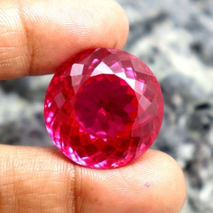 May include: A bright pink, faceted gemstone with a round shape.
