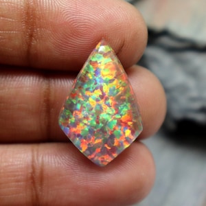 May include: A teardrop-shaped opal cabochon with a rainbow of colors, including red, orange, yellow, green, blue, and purple. The opal is set in a clear, faceted setting.