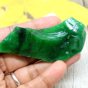Può includere: Un pezzo di vetro verde vibrante di forma irregolare, con una qualità traslucida e una consistenza superficiale liscia e lucida. L'oggetto presenta profonde tonalità smeraldo e sottili variazioni nell'intensità del colore lungo i bordi frastagliati.