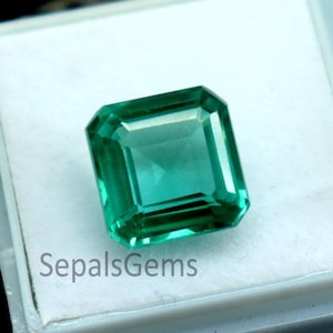 May include: A vibrant, emerald-cut green gemstone displayed in a white plastic case. The gemstone has a rectangular shape with beveled edges. The case is open, revealing the gem against a white background. The text "SepalsGems" is visible.