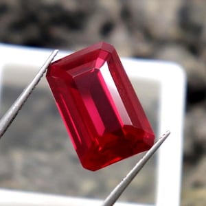 Può includere: Una pietra preziosa rosso scuro con taglio smeraldo rettangolare. La pietra preziosa è tenuta da una pinzetta.