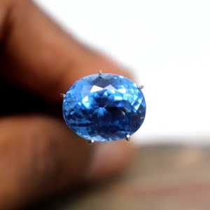 May include: A bright blue oval-shaped gemstone with facets, held in place by prongs.