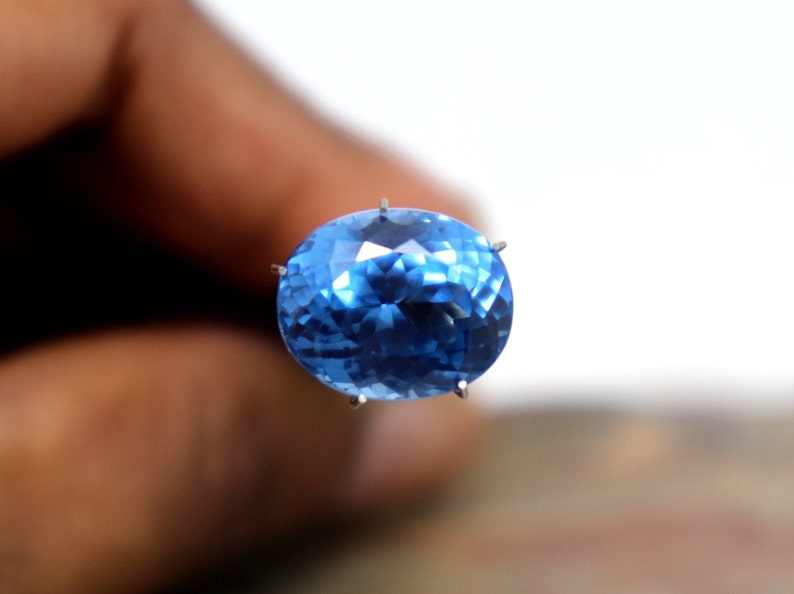 May include: A bright blue oval-shaped gemstone with facets, held in place by prongs.