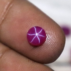 May include: A close-up of a pink star sapphire gemstone with a white star in the centre.