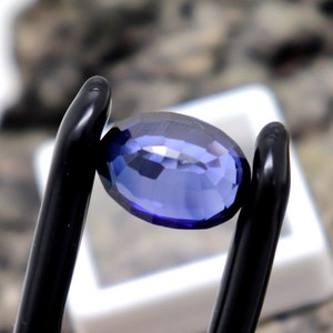 May include: A deep blue oval-shaped gemstone held in a pair of black tweezers.