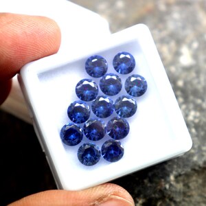 May include: A white box filled with round, blue gemstones. The gemstones are arranged in a circular pattern.