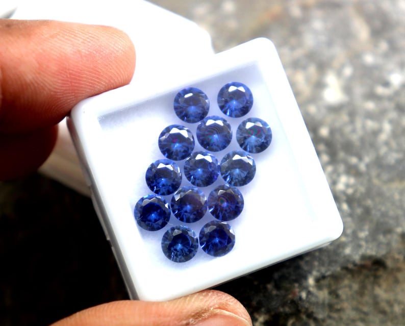 May include: A white box filled with round, blue gemstones. The gemstones are arranged in a circular pattern.