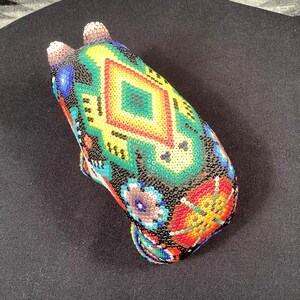 May include: A beaded animal figurine with a black, green, yellow, red, and blue geometric pattern. The figurine is made of small, colorful beads.