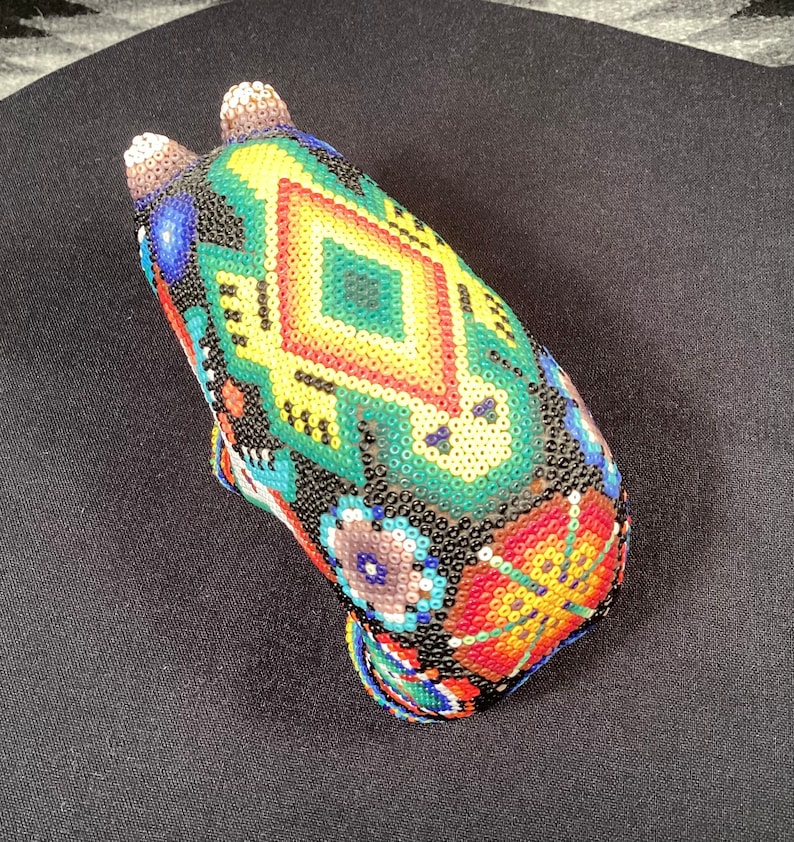 May include: A beaded animal figurine with a black, green, yellow, red, and blue geometric pattern. The figurine is made of small, colorful beads.