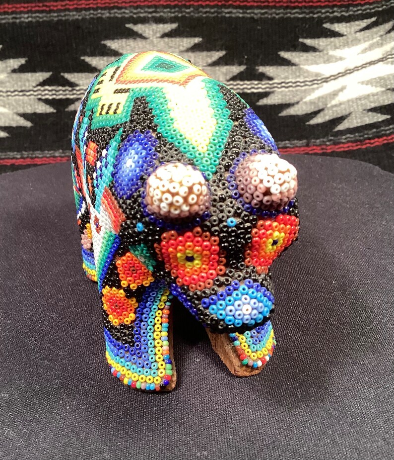 May include: A beaded bear figurine with a colorful geometric pattern. The bear is black with blue, green, red, yellow, and white beads.