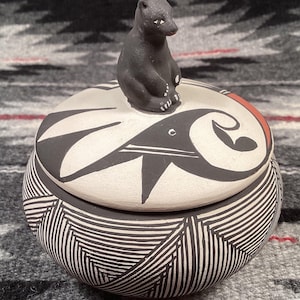 May include: A black and white ceramic jar with a lid featuring a black bear figurine. The jar has a geometric pattern and the lid has a swirl design.