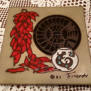 May include: Square ceramic tile with a Southwestern design. Features a cluster of red chili peppers, a black and brown circular design, and a white pot with a brown and turquoise design. Signed "83 Tessedre".