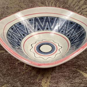 May include: A white ceramic bowl with a blue and red geometric design. The bowl has a square shape and a slightly rounded bottom.