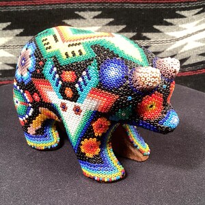 May include: A colorful beaded bear figurine with a black background and intricate patterns in shades of blue, red, green, and yellow.