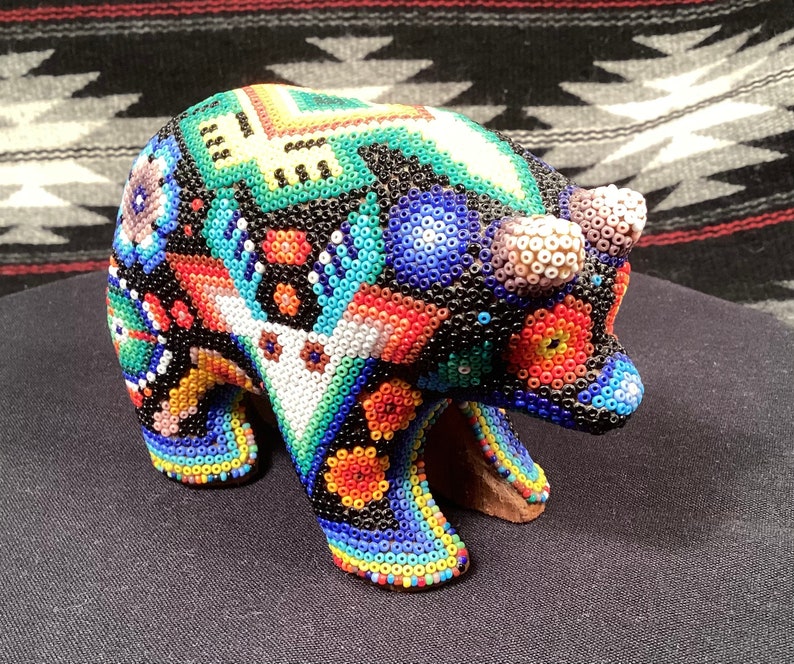 May include: A colorful beaded bear figurine with a black background and intricate patterns in shades of blue, red, green, and yellow.
