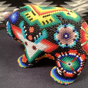 May include: A colorful beaded bear figurine with a geometric pattern. The bear is made of small, colorful beads and has a black base.