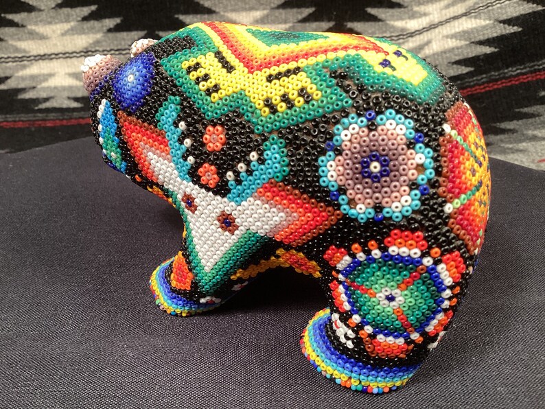 May include: A colorful beaded bear figurine with a geometric pattern. The bear is made of small, colorful beads and has a black base.