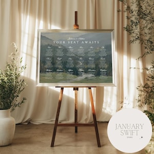 May include: A rectangular wedding seating chart sign with a silver frame displayed on a wooden easel. The sign features a landscape photograph of rolling hills and the text "Julianna & Nathan" and "YOUR SEAT AWAITS" above eighteen numbered tables.