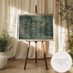May include: A wedding seating plan displayed on a wooden easel. The chart, framed in silver, features a Monet-style painting with guest names and table assignments. The text "YOUR SEAT AWAITS" is at the top. The easel is made of brown wood.