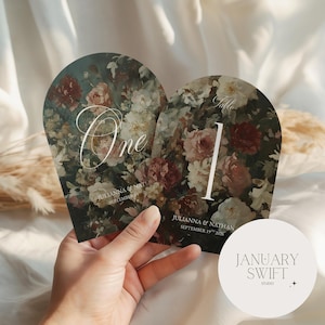 May include: Two floral table cards with the numbers "One" and "1" in white. The cards feature a dark background with a vintage floral design in shades of red, pink, and cream. The names "Julianna & Nathan" and the date "September 19th 2026" are printed on the cards.