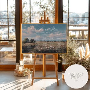 May include: A wooden easel supports a framed seating plan with the text "Our Favorite People" and "Your Seat Awaits." The chart features a landscape scene and guest names. The January Swift Studio logo is visible.
