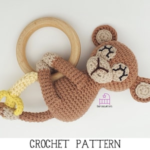 May include: A crocheted monkey toy with closed eyes and a banana attached to its hand. The monkey is holding onto a wooden teething ring.